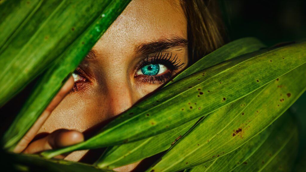 A woman face and eye peeking through the leaves of a plant