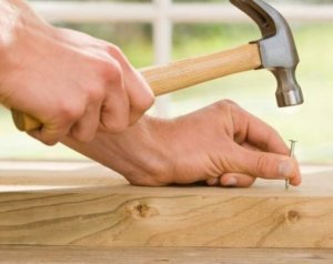 two hands holding a hammer and a nail to hammer into a board of wood